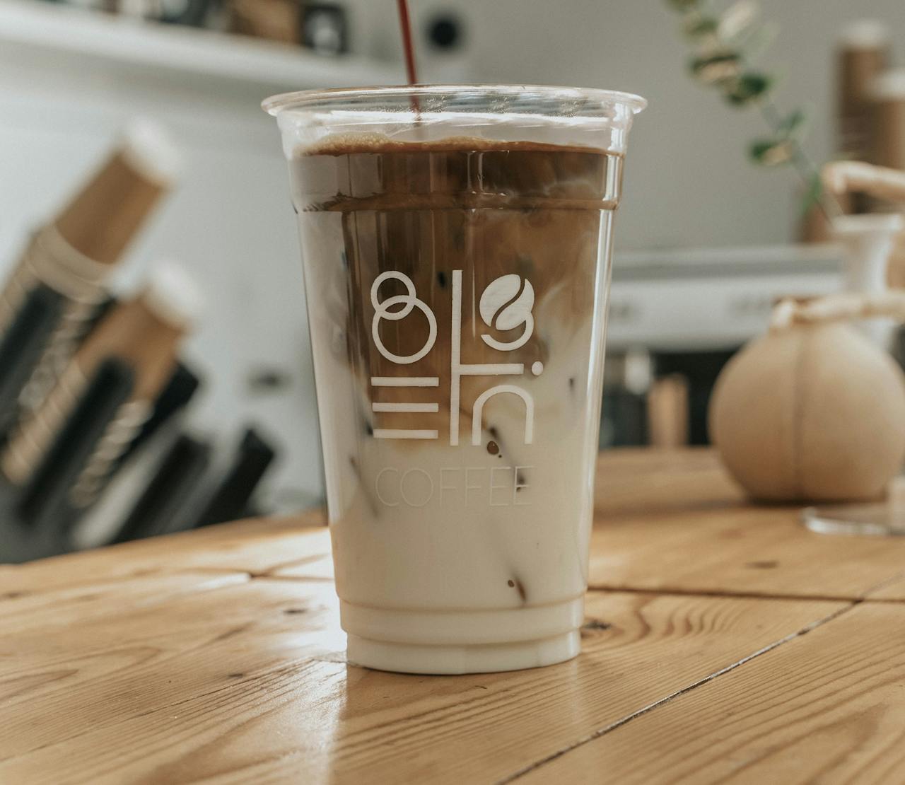 Close-up of a refreshing iced coffee in a stylish clear cup on a wooden table in a cozy coffee shop setting.